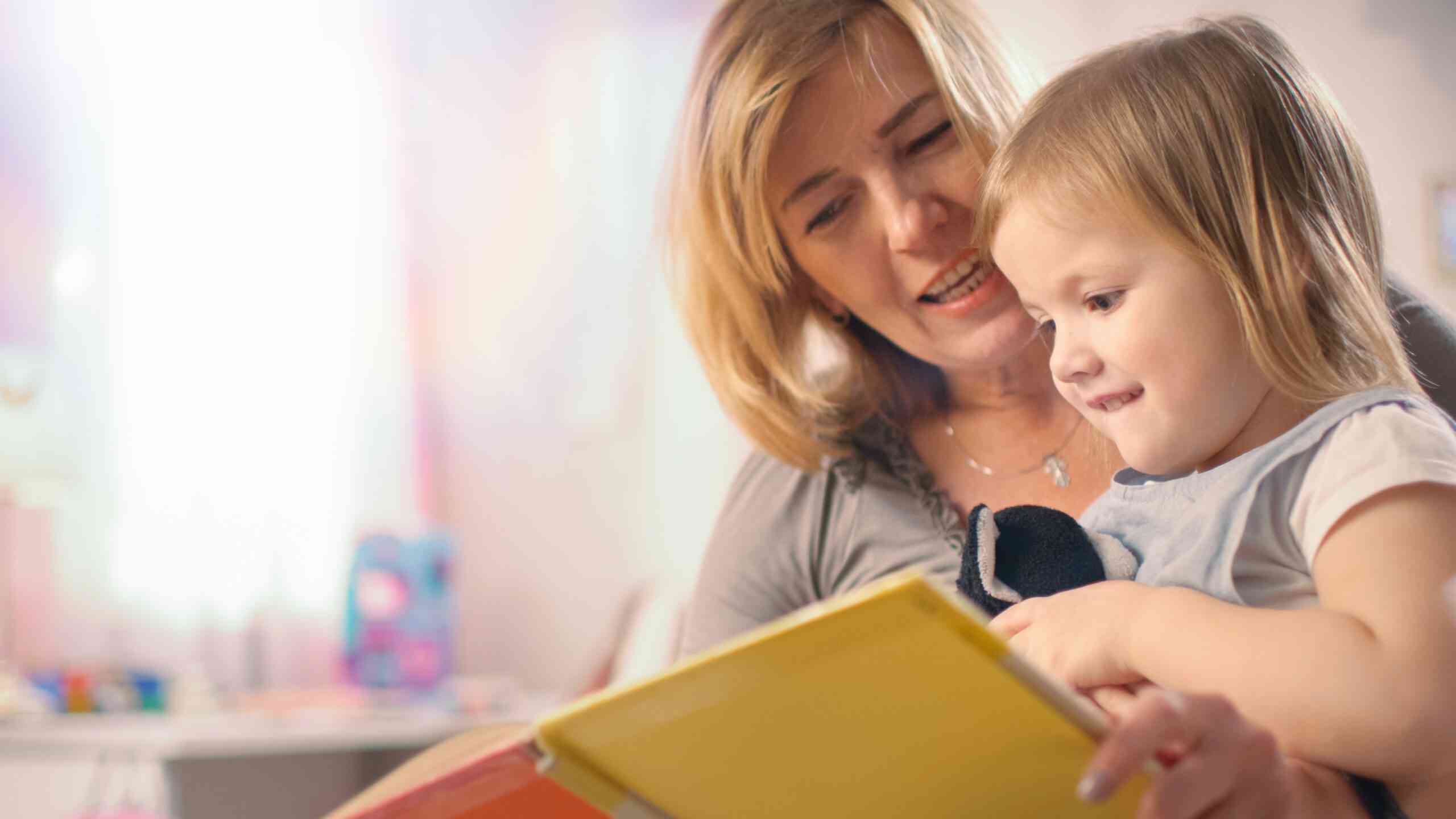 Close-up Shot of a Beautiful Young Mother and Her Cute Little Daughter Read Children's Book Together. Children's Room is Pink and Full of Toys.